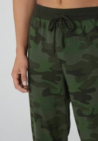 Groene loungebroek met camouflagepatroon, voorzien van een elastische tailleband en zachte stof. Het patroon bevat donkere en lichte groentinten.