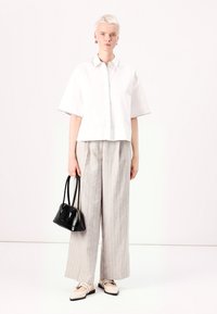 Blusa bianca a maniche corte con cucitura decorativa, abbinata a pantaloni larghi a righe grigie. Una borsa nera e scarpe beige completano l'outfit.