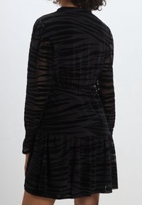 Svart klänning med tigerstrimmönster, långa genomskinliga ärmar, åtsittande midja och en utsvängd volangsläpp. Mjuk textur och lätt material.