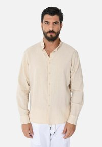 Camicia a maniche lunghe beige realizzata in tessuto leggero, con colletto abbottonato, caratterizzata da una vestibilità rilassata e maniche arrotolabili.