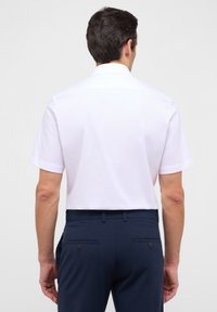 Witte short-sleeve button-up shirt met een gestructureerde kraag; gedragen met marineblauwe broek met twee achterzakken en knoopaccenten.