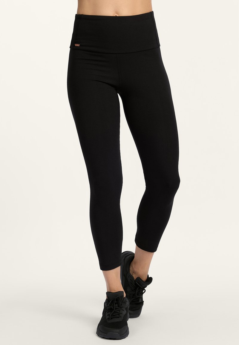 Zwarte high-waisted leggings met een gladde textuur en een aansluitend ontwerp, gecombineerd met zwarte sportschoenen met gaasdetail.