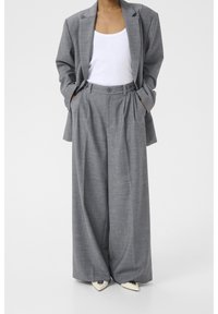 Harmaa räätälöity bleiseri ja leveälahkeiset housut teksturoidusta kankaasta. Yllä valkoinen toppi, ja jalassa kärjelliset kengät.