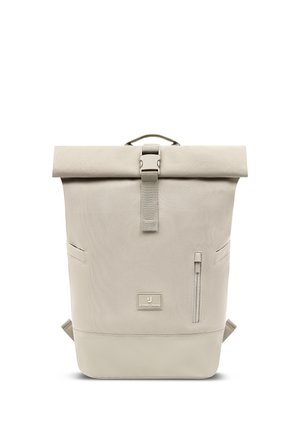 Mochila beige con cierre enrollable, hebilla frontal, correas laterales, bolsillo vertical con cremallera y parche con la marca "Johnny Urban" en el centro delantero.