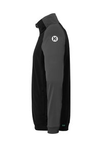 Sort og grå jakke med opretstående krave, tekstureret stof, lomme med lynlås og et cirkulært logo på venstre skulder.