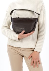 Brūna ādas plecu soma ar apaļu formu, aprīkota ar rāvējslēdzēja aizdari un noņemamu siksniņu. Soma ir gludas tekstūras.