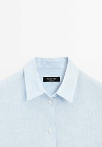 Chemise à fines rayures bleu clair et blanc avec col et boutons, étiquette noire portant la mention Massimo Dutti.