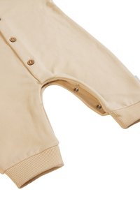 Un body beige en tissu doux, avec des détails de boutons, un col rond, des manches longues et des pressions aux ouvertures des jambes.
