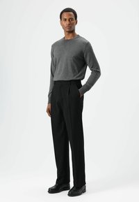 Chemise grise à manches longues et col rond, associée à un pantalon noir plissé et des chaussures noires. La tenue présente un design épuré avec une texture douce.