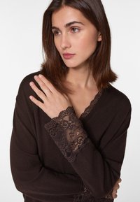 Braunes Langarmoberteil mit Spitzenbesatz an den Bündchen und am Ausschnitt, gefertigt aus einem weichen Material mit glatter Textur.