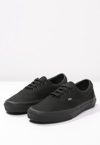 Černé plátěné tenisky s nízkým designem, gumovou podrážkou a šesti otvory na tkaničky. Výrazné logo Vans na boku.