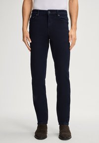Jeans dritti blu navy con una texture liscia, design a cinque tasche e dettagli di cucitura sottili. Indossati con stivali alla caviglia marroni.