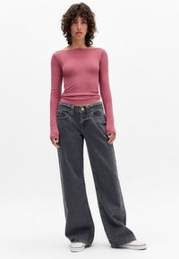 Aansluitend langshirt in roos met boot hals, gecombineerd met wijde donkergrijze gestreepte spijkerbroek. Model draagt witte sneakers.