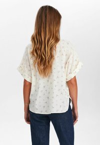 Floral blouse in lightweight fabric, off-white with small pink flowers, short sleeves, side slits, and a relaxed fit.