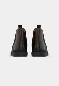 Brown leather ankle boots with elastic side panels, pull tabs, and black rubber soles, featuring a smooth texture and subtle stitching details.