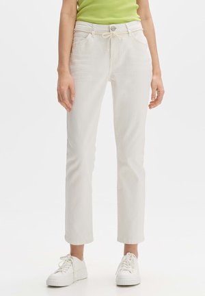 White cotton pants with a drawstring waist, front pockets, and straight-leg design, paired with white sneakers and a green top.