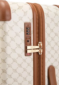 Valigia rigida con motivo a rilievo beige, dettagli marroni, doppie cerniere e lucchetto a combinazione. Logo del marchio visibile sulle cerniere.