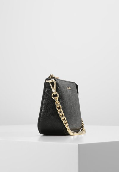 Sac à main en cuir noir avec une finition texturée, dotée d'une bandoulière en chaîne dorée et d'une fermeture à glissière sur le dessus. Forme compacte et trapézoïdale.