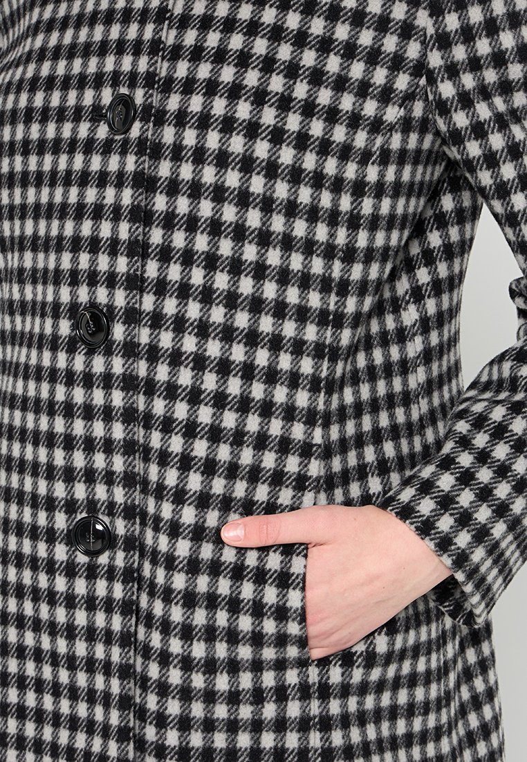 Zwart-wit houndstooth-geprint jasje met lange mouwen, knopen aan de voorkant en zijzakken, gemaakt van een gestructureerde stof.