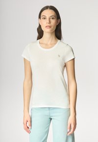 T-shirt bianco aderente con maniche corte e scollatura rotonda; presenta un piccolo logo dorato sul petto; texture liscia, tessuto leggero.