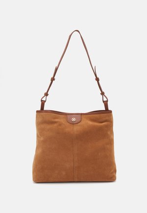 Sac fourre-tout en daim marron avec une texture lisse, doté d'une bandoulière en cuir marron et d'un détail logo circulaire près du haut. Design simple et sans ornements.
