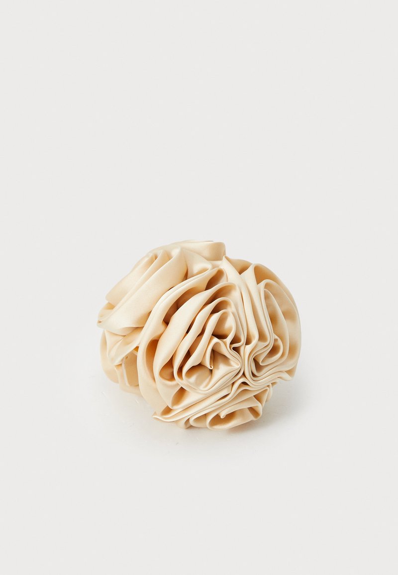Scrunchie de cabelo em cetim bege, em forma circular, texturizado com pregas volumosas, brilho suave, sem peças ou detalhes visíveis, material leve.