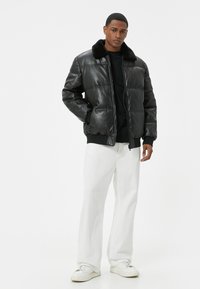 Veste en simili cuir noire avec un design matelassé, dotée d'un col en fourrure noire. Associée à un pantalon blanc et des baskets blanches.
