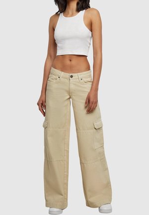 Pantalons cargo beiges avec des jambes larges, poches avant et poches cargo sur les côtés. Associés à un haut court blanc ajusté. Tissu lisse et léger.