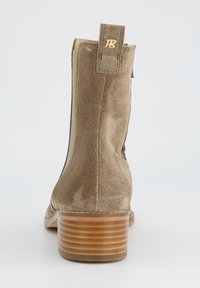 Kerge pruun nubukist pahkluumoodustis, millel on sile tekstuur, ümardatud nina, ribaga puidust konts ja kuldne logo tagaosas.