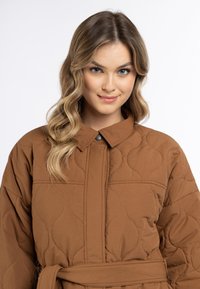 Bruine gewatteerde jas met een kraag, een textuurpatroon en een strikceintuur in de taille. De stof heeft een gladde afwerking.