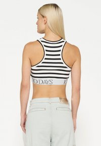 Zwart-wit gestreepte crop top met een racerback ontwerp, voorzien van een gebrandmerkt elastieken band aan de onderkant. Het materiaal lijkt ribbelig.