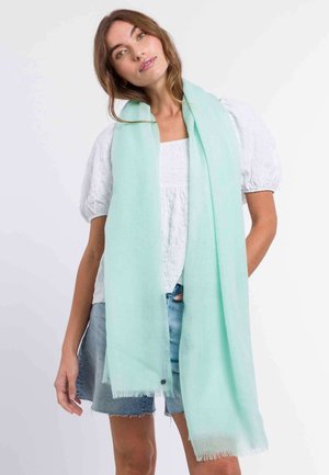 Sciarpa verde menta chiaro realizzata in tessuto morbido e leggero, con bordi frangiati e una texture liscia, indossata in modo sciolto.