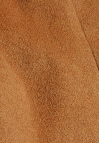 Close-up van zacht, pluizig kamelbruin stof met zichtbare textuur en diagonale naadlijn.