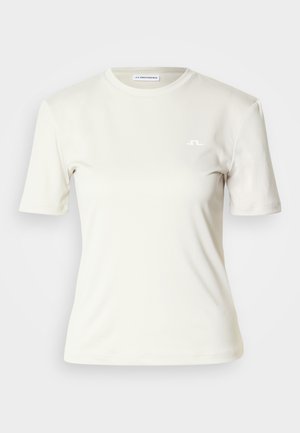 Kortermet skjorte i lyst beige stoff med glatt tekstur; har en liten hvit logo på brystet og rund hals.