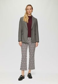 Grau doppelreihiger Blazer über einem bordeauxfarbenen gerippten Pullover, kombiniert mit gemusterten, cropped Hosen in Schwarz, Weiß und Rot. Schwarze Slipper.
