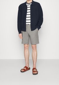 Námořnická bunda na zip, tričko s bílými a námořnickými pruhy, světle šedé šortky, hnědé sandály se dvěma popruhy.