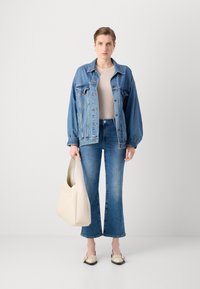 Jeansjakke med pufferm, ribbet beige topp, bukser med vidde i blått og beige skulderveske; iført to-fargede sko med nagler.