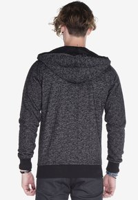 Kapuzensweatshirt aus schwarzem und grauem Melange-Stoff, mit strukturiertem Finish, gerippten Bündchen und Saum. Das Innenfutter besteht aus einem glatten Material.