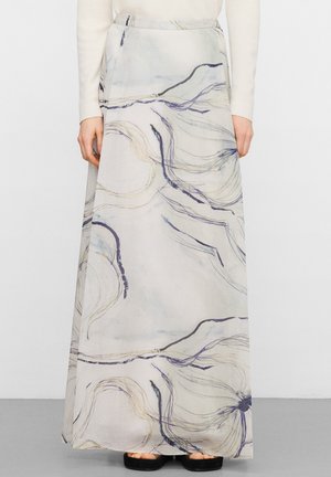 Gonna lunga bianca con motivi astratti di linee ondulate nere e beige, indossata con una maglia bianca a maniche lunghe e sandali neri.