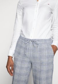 Ljusblå rutiga byxor med elastisk dragsko i midjan, framfickor och lös passform, tillsammans med en vit skjorta med knappar.