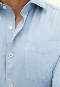 Helles blaues Hemd mit Knöpfen aus einem glatten Stoff. Verfügt über einen Kragen, weiße Knöpfe und eine Brusttasche mit subtilen Nähdetails.