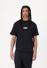 Black cotton t-shirt with short sleeves, featuring a central white and red graphic logo. Simple, relaxed fit and a round neckline.