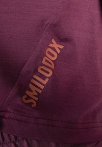 Dieprode activewear stof met een gladde textuur, voorzien van een verhoogd bruin "SMILODOX" logo. Inclusief een gathered zoomdetail.