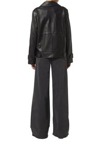 Schwarze Lederjacke mit breitem Kragen, großen Knopfdetails und lockerer Passform, kombiniert mit hochgeschnittenen, weit geschnittenen, dunkelgrauen Jeans.