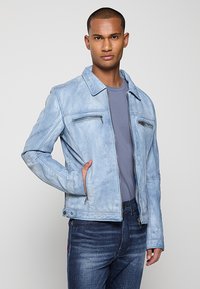 Veste en cuir bleu clair avec un col classique, fermeture éclair à l'avant, deux poches poitrine et une coupe ajustée, assortie à un t-shirt gris et un jean en denim.