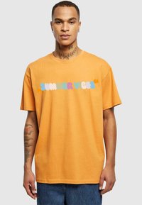 Orange bomulds T-shirt med et multifarvet "SUMMER VIBES" grafik over brystet. Korte ærmer, afslappet pasform og rund halsudskæring.