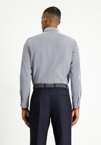 Camisa de manga larga para hombre en azul claro con finas rayas blancas, con cuello estándar y puños ajustados, llevada con pantalones azul marino y cinturón con estampado.