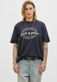 Zwarte katoen T-shirt met witte logo-print, losse pasvorm, korte mouwen. Draag het met lichtblauwe denim jeans en een zwarte riem met zilveren hardware.