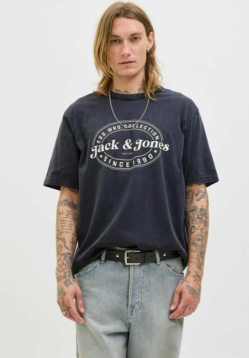 Zwarte katoen T-shirt met witte logo-print, losse pasvorm, korte mouwen. Draag het met lichtblauwe denim jeans en een zwarte riem met zilveren hardware.