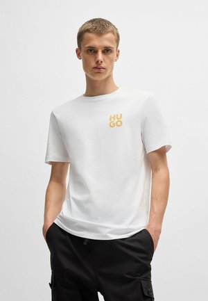 T-shirt en coton blanc à manches courtes, avec un logo "HUGO" jaune sur la poitrine gauche. Texture lisse, col rond simple.